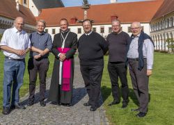 Eine Gruppe von Geistlichen steht bei sonnigem Wetter im Innenhof von Stift Reichersberg zusammen.