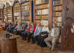 Ein junger Mann hält einen Vortrag vor einer Besuchergruppe in der Bibliothek des Stifts Reichersberg.