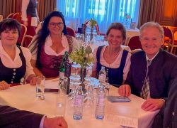 Eine Gruppe von Menschen in traditioneller Tracht sitzt lächelnd an einem Tisch beim Ball der Oberösterreicher in Wien.