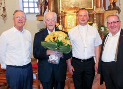 Vier Männer lächeln in einer Kirche beim Priesterjubiläum von H. Wolfgang im Stift Reichersberg, einer hält einen Blumenstrauß.