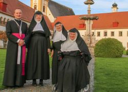 Eine Gruppe von Augustiner-Chorfrauen und einem Priester posiert lächelnd vor dem historischen Stift Reichersberg.