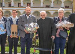 Eine Gruppe von Gratulanten überreicht Geschenke zum 90. Geburtstag im Garten von Stift Reichersberg.
