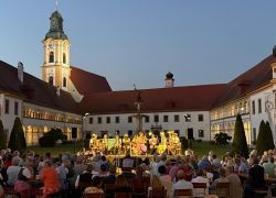 Eine abendliche Musikveranstaltung findet im malerischen Innenhof von Stift Reichersberg statt, umgeben von zahlreichen Zuschauern.