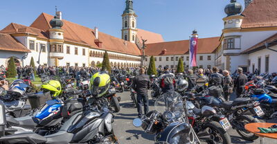 Motorradfahrer versammeln sich zur Bikerwallfahrt vor dem historischen Stift Reichersberg an einem sonnigen Tag.