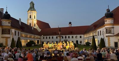 Eine abendliche Musikveranstaltung findet im malerischen Innenhof von Stift Reichersberg statt, umgeben von zahlreichen Zuschauern.